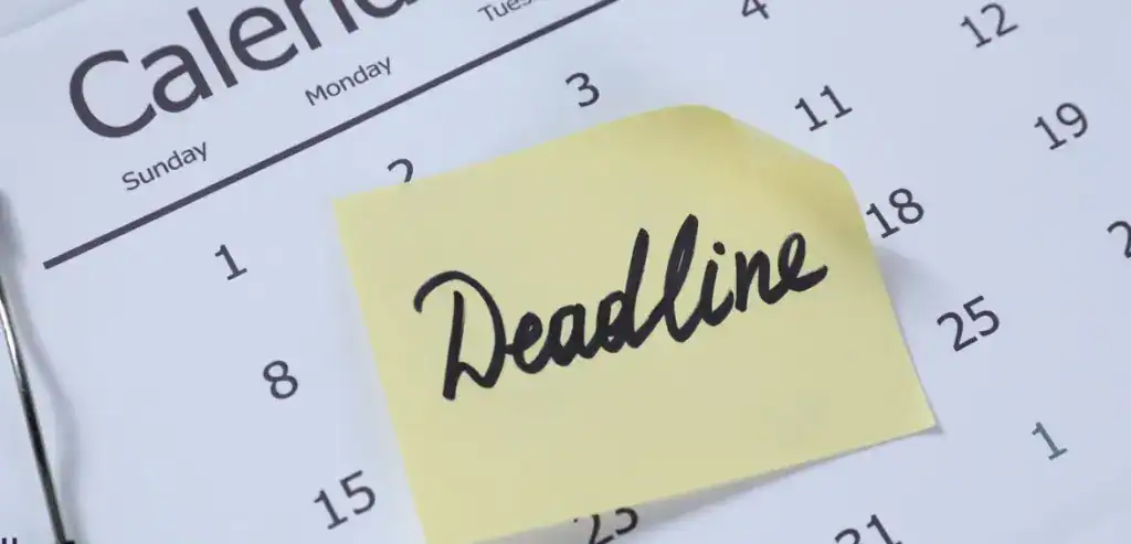 A close-up of a monthly calendar with a yellow sticky note in the center that has the word "Deadline" written on it in black cursive, representing important return dates or scheduling